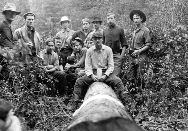 black and white photo of forester students sitting on and standing around a downed tree