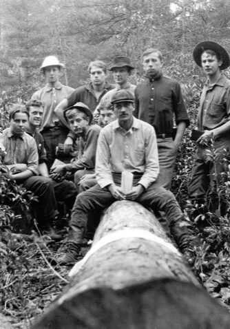 black and white photo of forester students sitting on and standing around a downed tree